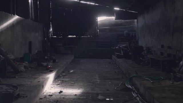 Dark abandoned farm building with light beaming through holes in walls and roof. Scary, eerie dark shadows. Cobwebs and dust cover random objects.
