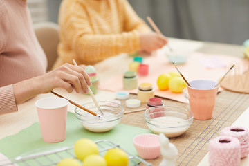 Obraz na płótnie Canvas Close up of unrecognizable mother and daughter painting Easter eggs pastel colors sitting at table in cozy kitchen interior, copy space