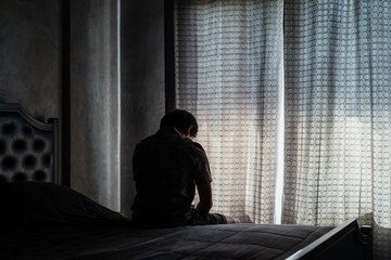 Lonely young man feeling depressed and stressed sitting head in hands in the dark bedroom, Negative emotion and mental health concept