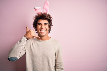 Young handsome man holding easter rabbit ears standing over isolated pink background smiling doing phone gesture with hand and fingers like talking on the telephone. Communicating concepts.