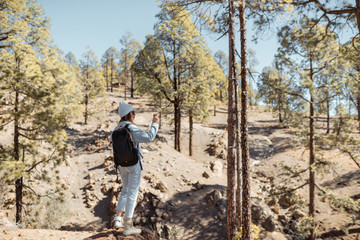 Stylish woman enjoying beautiful landscapes on volcanic rocks in the pine woods, traveling high in the mountains on Tenerife island, Spain