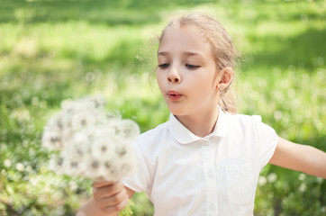 A girl of preschool or primary school age with dandelions in her hand in a summer meadow.