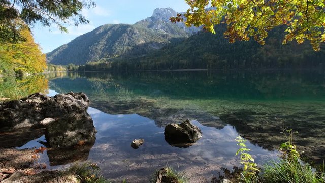 Sunny idyllic autumn alpine view. Peaceful Langbathseen lake with mountain  reflections and small school of fish, Upper Austria. Sunlight twinkling on tree foliage from water ripples reflections.