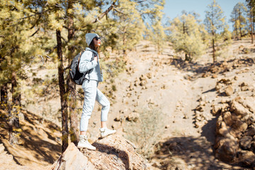 Stylish woman enjoying beautiful landscapes on volcanic rocks in the pine woods, traveling high in the mountains on Tenerife island, Spain
