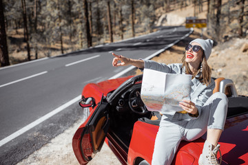 Woman enjoying road trip, sitting with map on the convertible car on the roadside in the volcanic mountain forest on Tenerife island, Spain