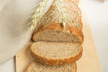 Sliced slices of coarse rye bread on a wooden cutting Board with a linen cloth and rye ears, the...