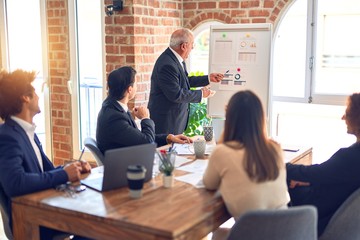 Group of business workers smiling happy and confident in a meeting. Working together looking at presentation using board and charts at the office.