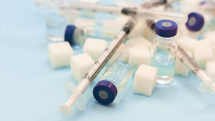 Sugar addiction, insulin resistance, unhealthy diet, sugar cubes, bottles of insulin and syringe for vaccination on blue background, diabetes protection medical concept, top view.