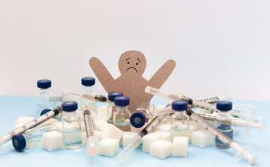 Sugar addiction, insulin resistance,   cardboard man surrounded by refined sugar cubes, syringe for vaccination and bottles of insulin on white background, diabetes protection medical concept.