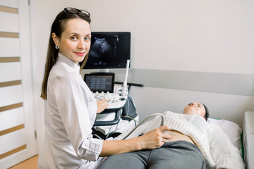 Obraz na płótnie Canvas Pretty female doctor operating modern ultrasound scanner while examining belly and bladder of her female patient