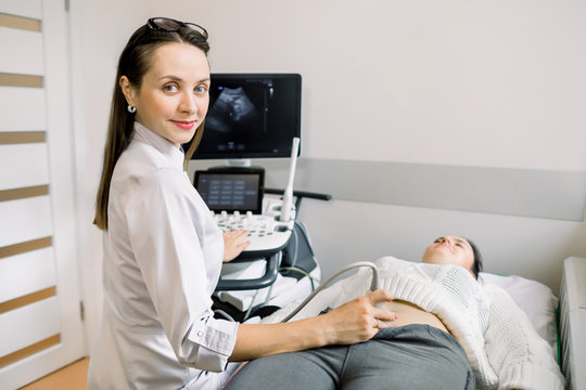 Pretty female doctor operating modern ultrasound scanner while examining belly and bladder of her female patient