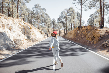 Lifestyle portrait of a stylish woman running on the beautiful mountain road, feeling happy and carefree while traveling. View from the backside