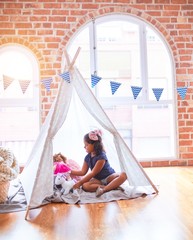 Beautiful toddler girl sitting on the floor playing with unicorn and doll inside  tipi at kindergarten © Krakenimages.com