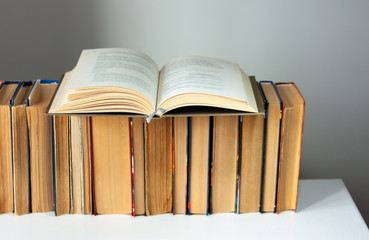 Open hardback book, diary, fanned pages on stack of books on white table in library. Books stacking. Back to school concept. Copy Space. Education learning background.