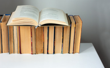 Open hardback book, diary, fanned pages on stack of books on white table in library. Books stacking. Back to school concept. Copy Space. Education learning background.