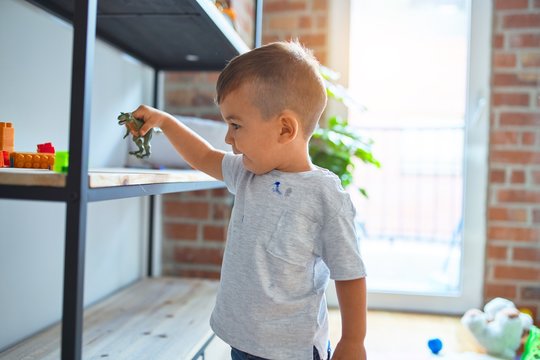 Adorable toddler smiling happy. Standing playing around lots of toys at kindergarten