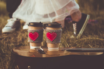 Romantic couple hugging while having picnic in sunset light. Coffee cup cozy knitted sleeve with felt red heart.