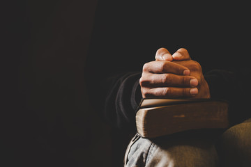 Soft focus on a hand of man while praying for christian religion with blurred of dark background.