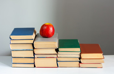 stack of hardback books on white table with red apple. Books stacking. Back to school concept. Copy Space. Education learning background.