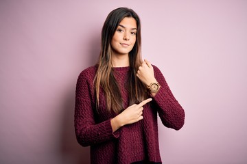 Young beautiful girl wearing casual sweater over isolated pink background In hurry pointing to...