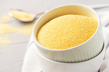 Dry uncooked polenta in bowls on the table, light background, space for text.