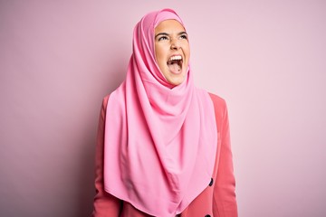 Young beautiful girl wearing muslim hijab standing over isolated pink background angry and mad screaming frustrated and furious, shouting with anger. Rage and aggressive concept.