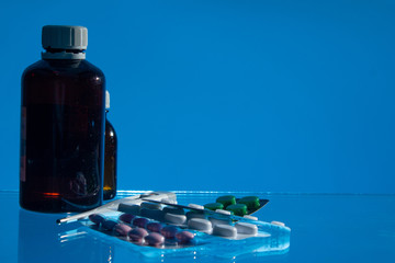 medical jars, thermometer, syringe, gauze mask and pills medicines, medicine on glass blue background close up. copy space