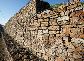 A drainage wall strengthens and holds an earthen slope. It consists of natural stones laid in a metal mesh.