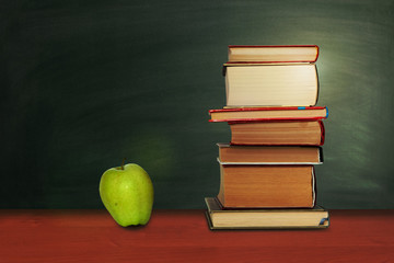 Back to school, pile of books and green apple with empty green school board background, education concept