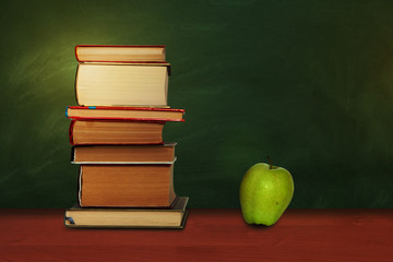 Back to school, pile of books and green apple with empty green school board background, education concept