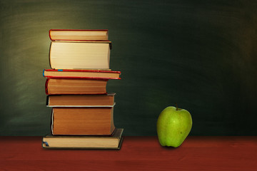 Back to school, pile of books and green apple with empty green school board background, education concept