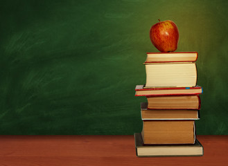 Back to school, pile of books and red apple with empty green school board background, education concept.