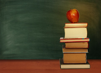 Back to school, pile of books and red apple with empty green school board background, education concept.