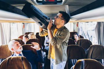 Good looking young man putting hand luggage in the top shelf in the bus.