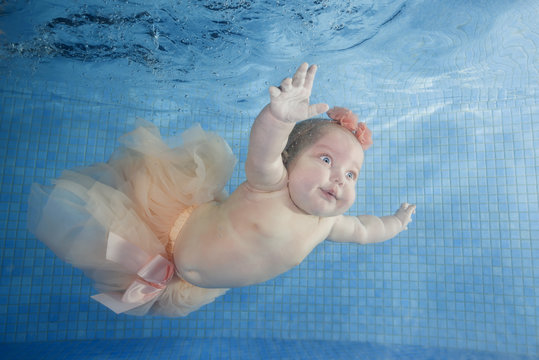 Cute chubby little girl dives underwater in a swimming pool