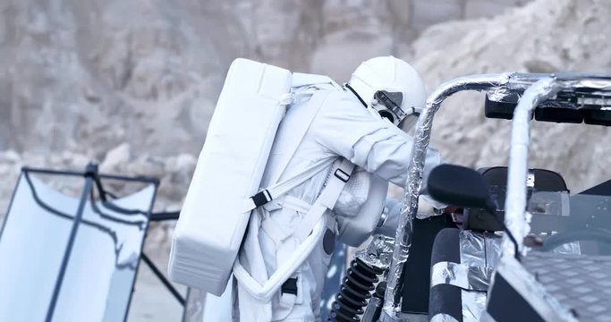 Astronaut in the full white armor repairing his moon rover or trying to turn on it while beng at the Moon or Mars. Outside.