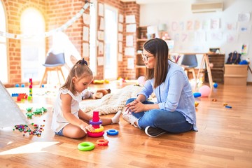 Caucasian girl kid playing and learning at playschool with female teacher. Mother and daughter at playroom playing with inteligence toys