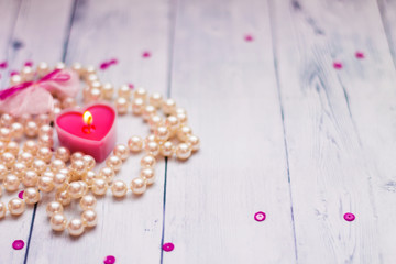 on a white wooden background red candle pearl beads
