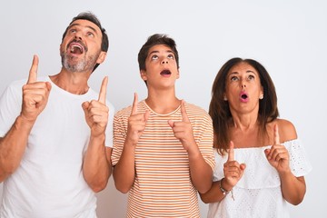 Family of three, mother, father and son standing over white isolated background amazed and...