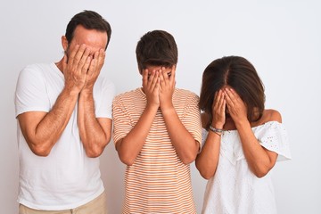 Family of three, mother, father and son standing over white isolated background with sad expression covering face with hands while crying. Depression concept.