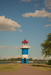 Blue and white lighthouse under a sky with clouds