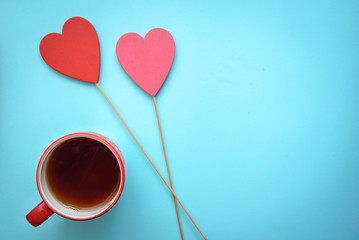 A mug of tea and two hearts on sticks on a blue background, with copy space