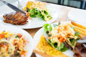 Close up knife and fork cutting grilled chicken steak set in white dish on wooden table background.Chicken grill, mashed potato, bread and salad.Restaurant menu.