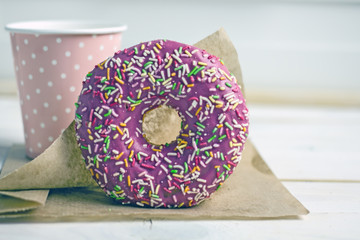 Sweet delicious donut in pink glaze with sprinkles on a wooden table on parchment paper