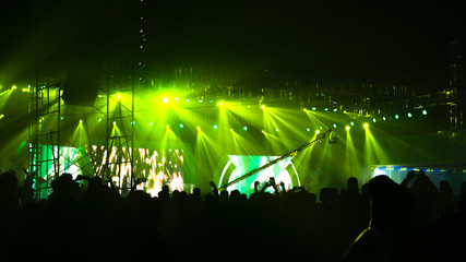 Silhouette spectator crowd people standing at concert performance pop rock music life event awards ceremony before green color stage light and enjoying cheering raising hands up in air facing band.