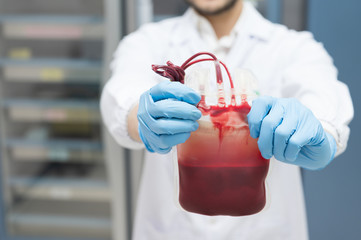 Selective focus scientist man hand holding red blood bag at blood bank unit laboratory.Young doctor selective fresh donor blood for transfusion.Save life and medical treatment concept.