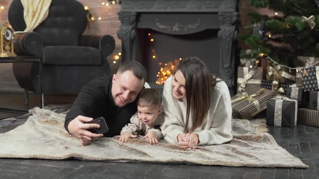 Young mother and father and their son are lying on a floor and watching some video on a phone, laughing and smiling.