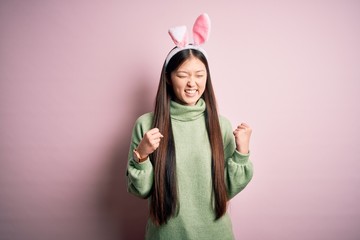Young asian woman wearing cute easter bunny ears over pink background excited for success with arms raised and eyes closed celebrating victory smiling. Winner concept.