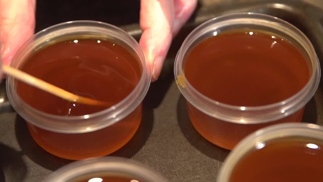 Thick dense freshly prepared homemade oil being stirred and stored in small containers. Close up.