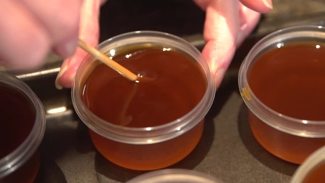 Thick dense freshly prepared homemade oil being stirred with wooden spatula and stored in small containers. Close up.